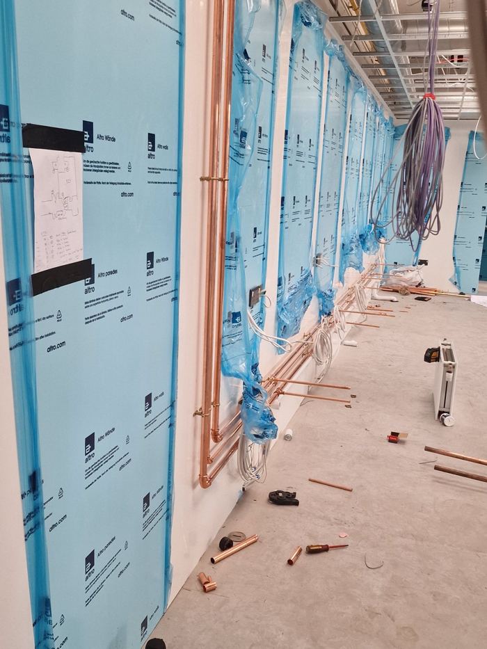 Copper pipework runs clipped along a newly boarded wall