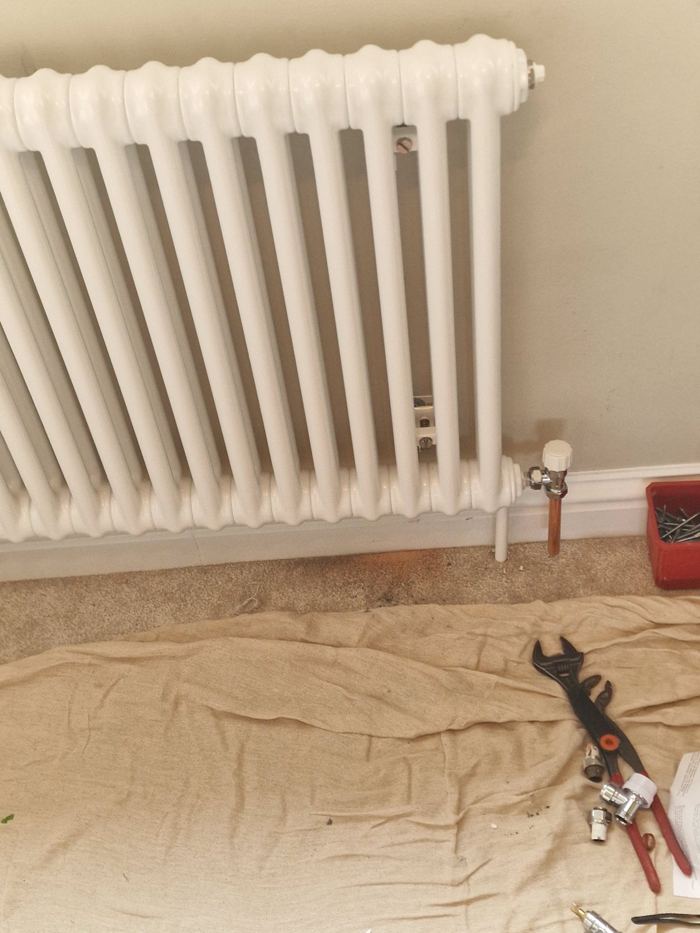 White column radiator being fitted, with dust sheet and tools laid out